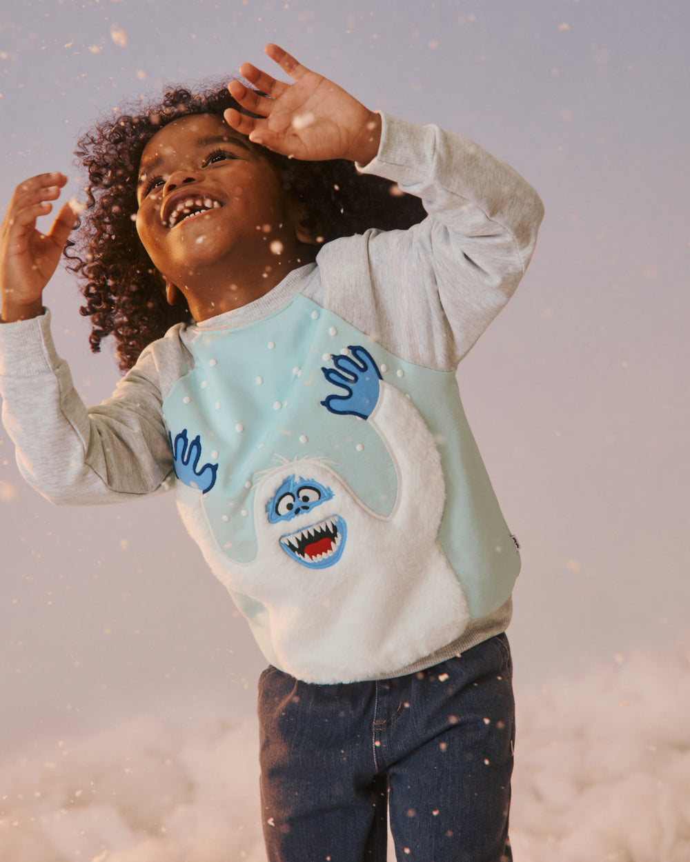 Young boy on a snowy studio set wearing the Rudolph Snowy Bumble Crewneck Sweatshirt