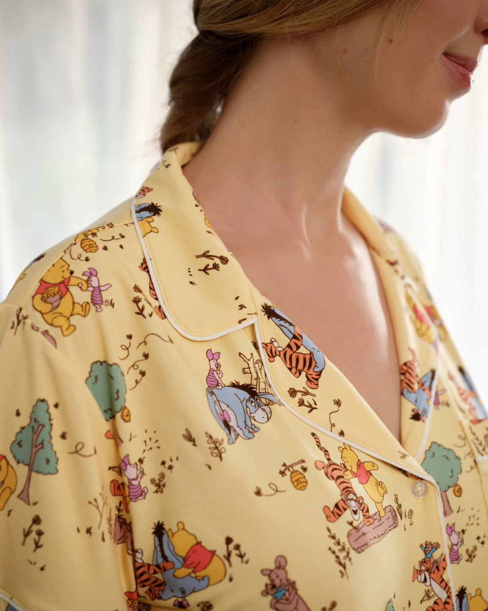 Close-up of a person wearing pale yellow pajama top with Winnie the Pooh and Tigger cartoon print, showing collar and upper chest area.
