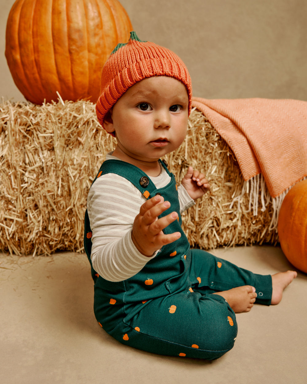 Sitting baby wearing the Pumpkin Sweater Beanie with Pumpkin print overalls