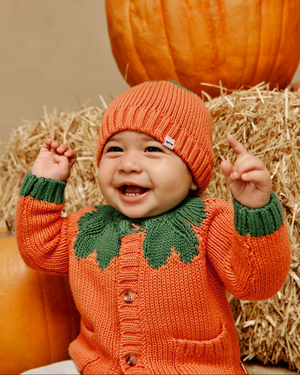Close up of baby wearing the Pumpkin Cardigan Sweater and Hat with a fall themed backdrop