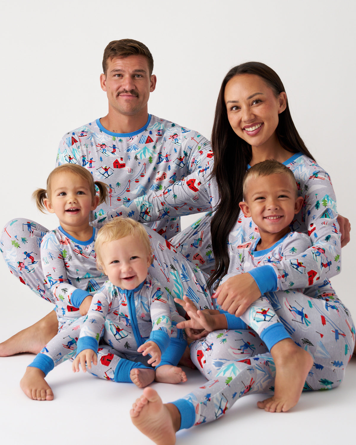 A family of five wearing matching light blue pajamas with a colorful space-themed print of rockets, planets, and stars, posed together against a clean white studio background.
