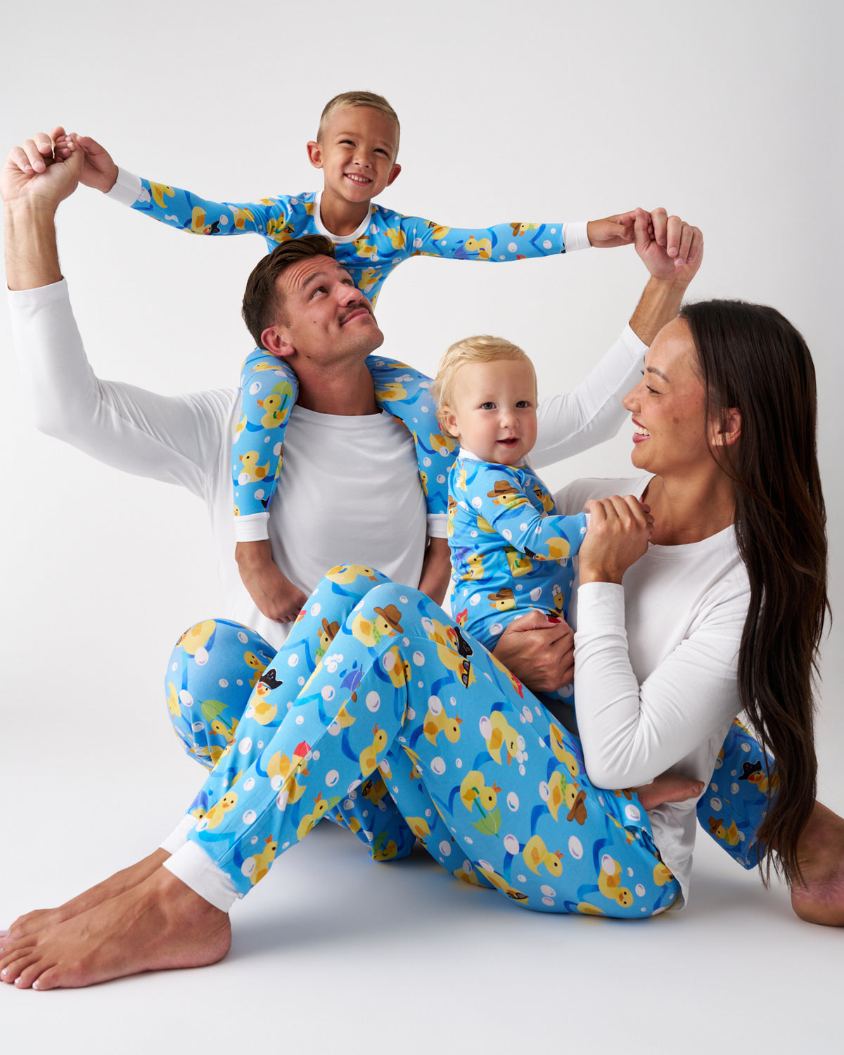 A family of four wearing matching blue pajamas with a playful dog print, posing together in a playful arrangement on a white studio background.