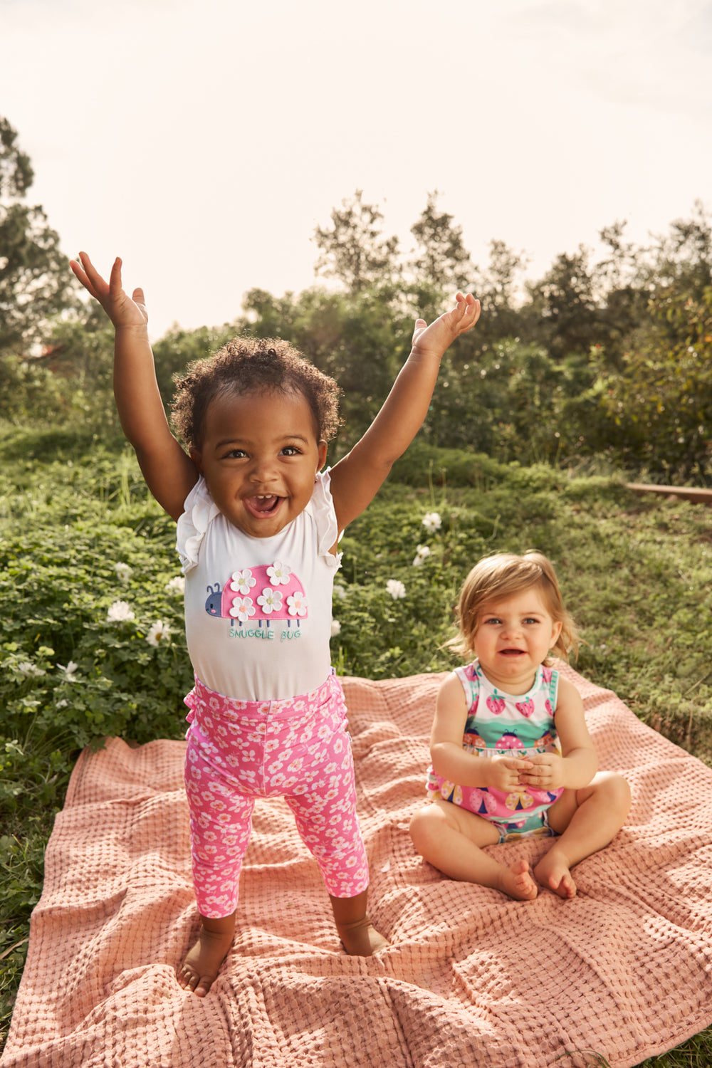 Two babies wearing styles from the Spring Play Capsule with a grass background