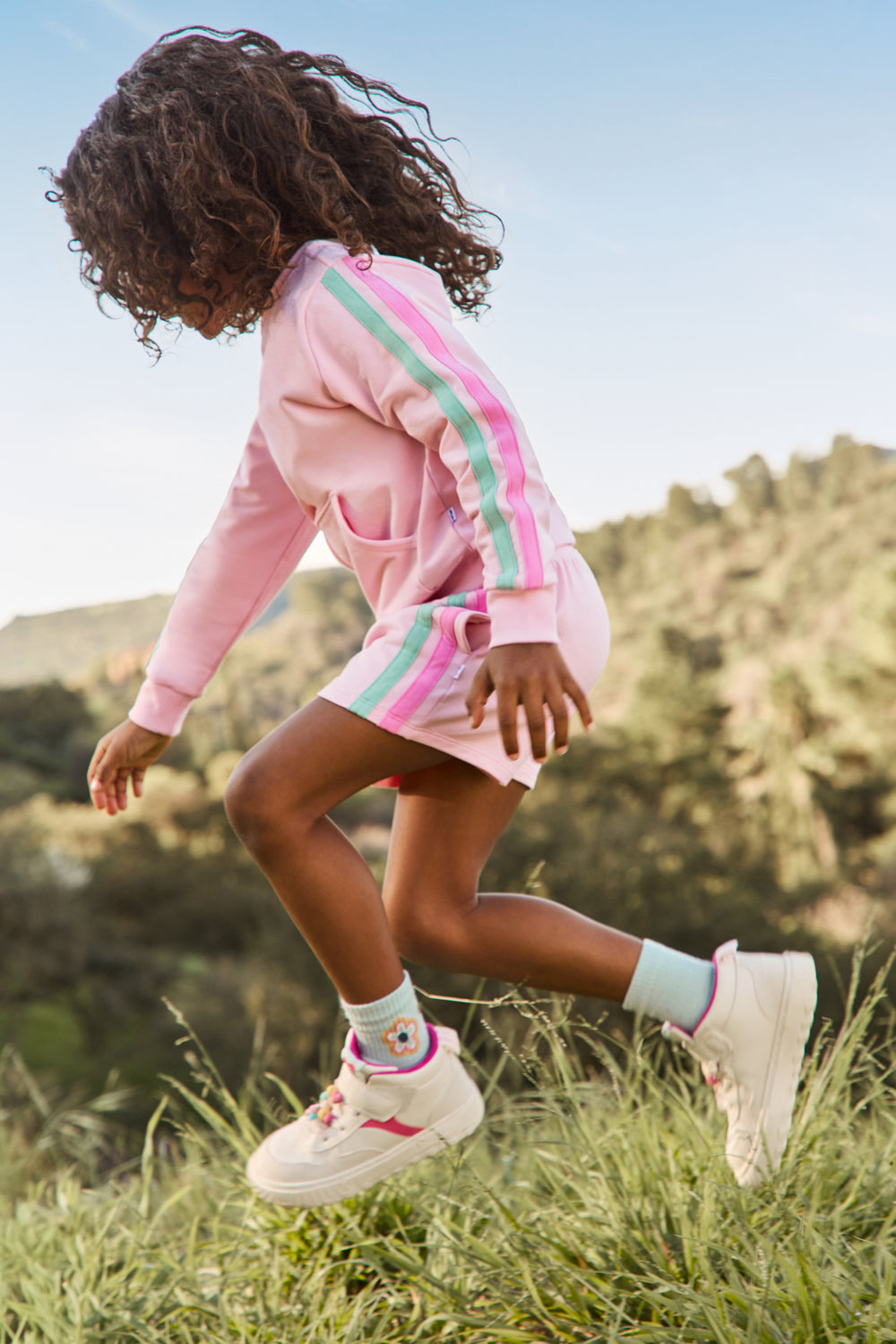 Girl running in the grass wearing the Pink Blossom Pocket Crewneck and shorts
