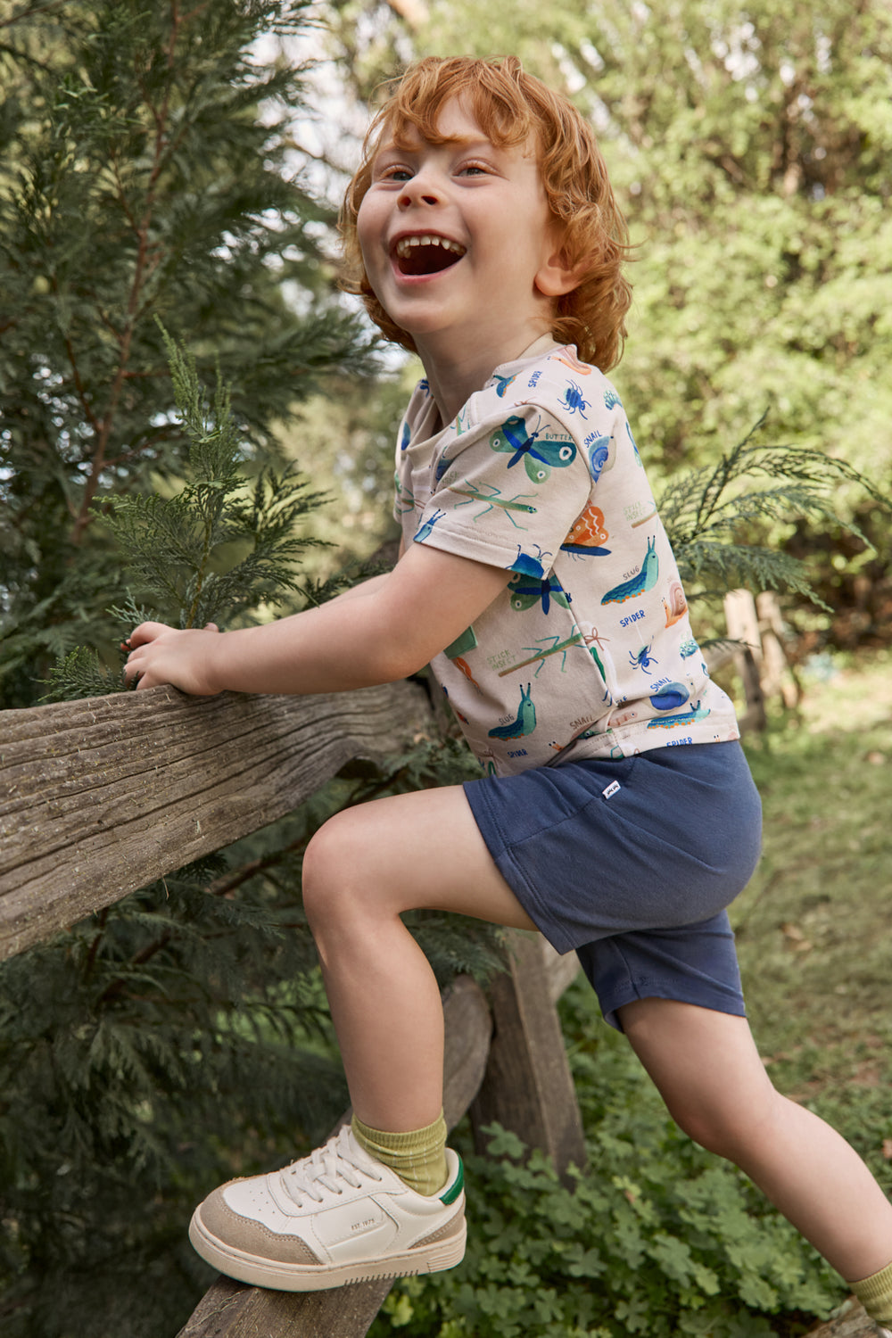 Boy climbing a fence wearing the Nature Notes Relaxed Pocket Tee with navy shorts