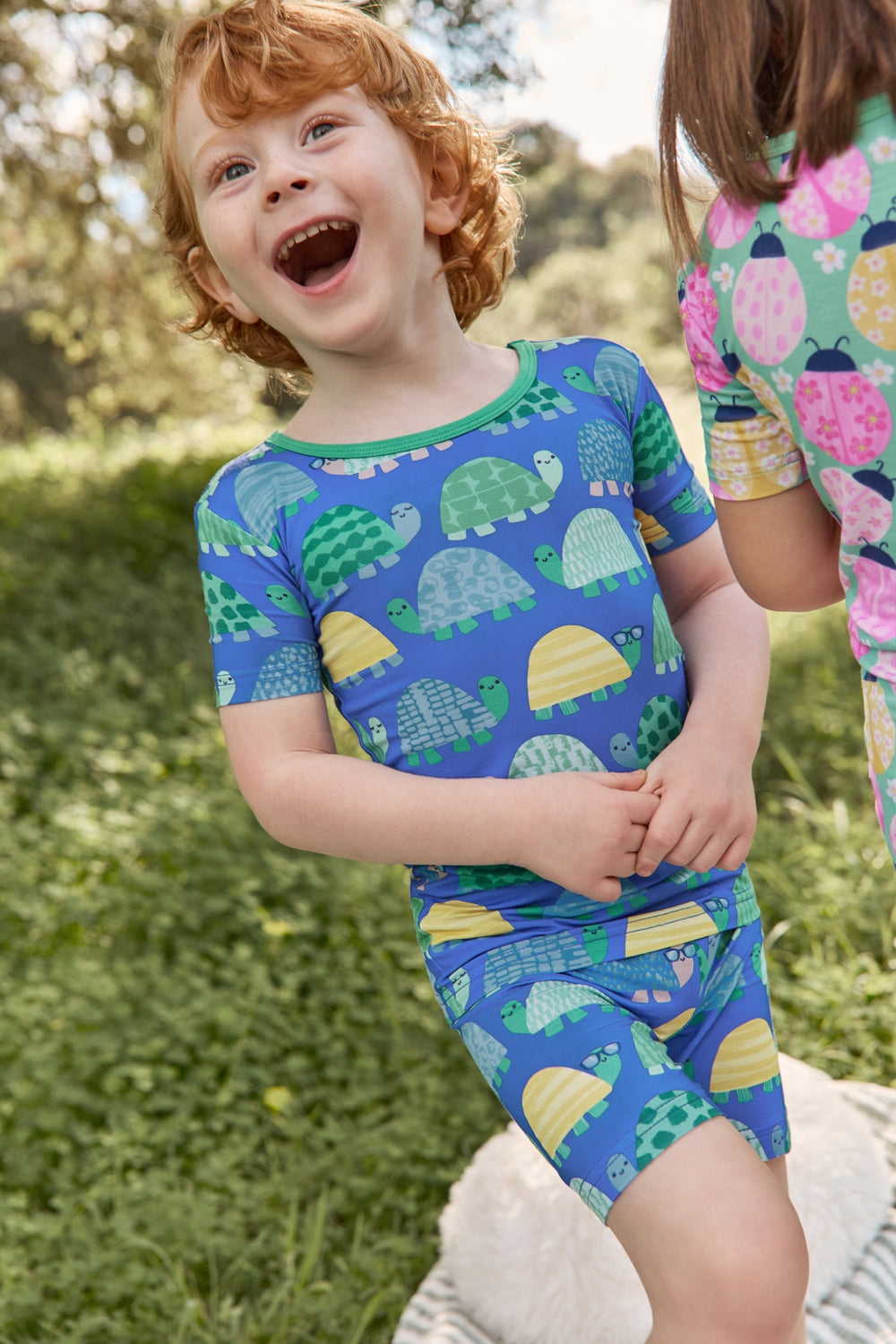 Boy wearing the Shell Parade Two-Piece Short Sleeve & Shorts Pajama Set with a grassy background