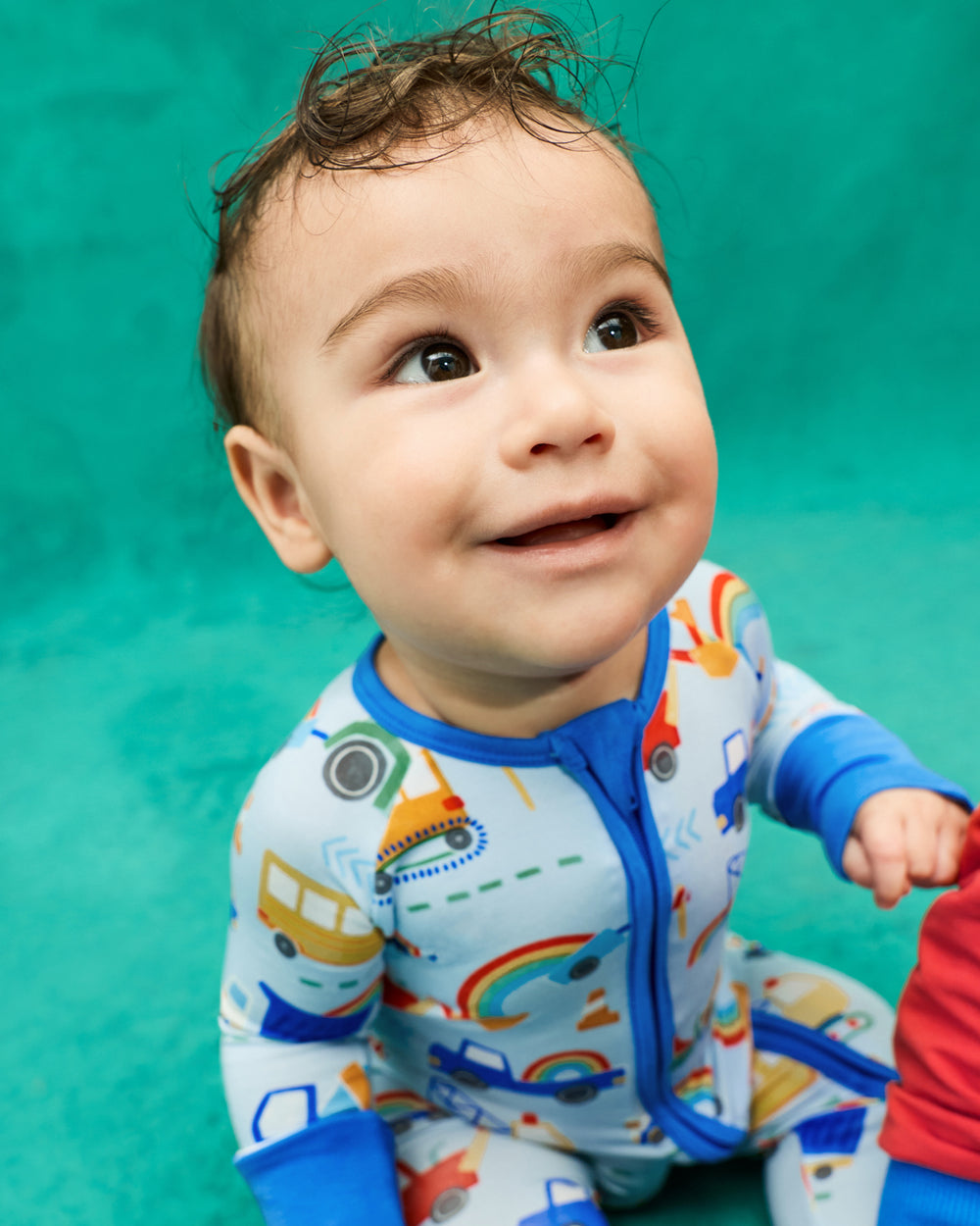 Baby wearing the Rainbow Trucks Zippy on a teal back drop