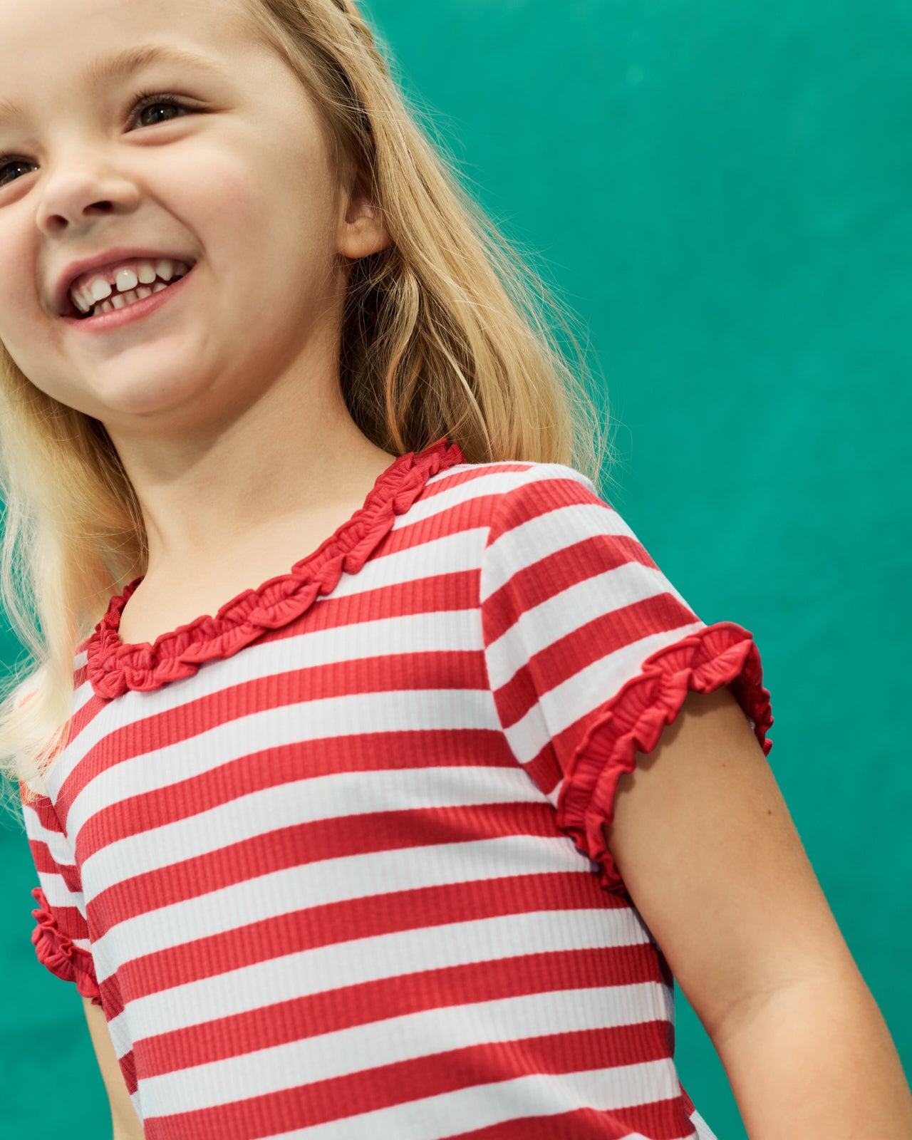 Girl wearing the Red Ember Stripe Ruffle Tee on a teal backdrop
