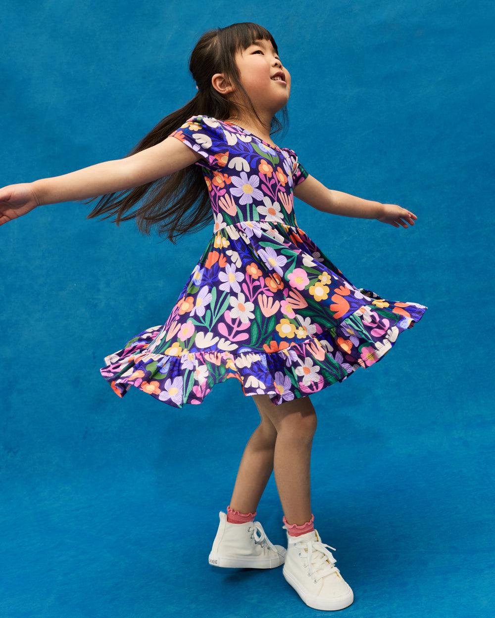 Twirling girl wearing the Wild Garden Ruffle Twirl Dress on a blue back drop