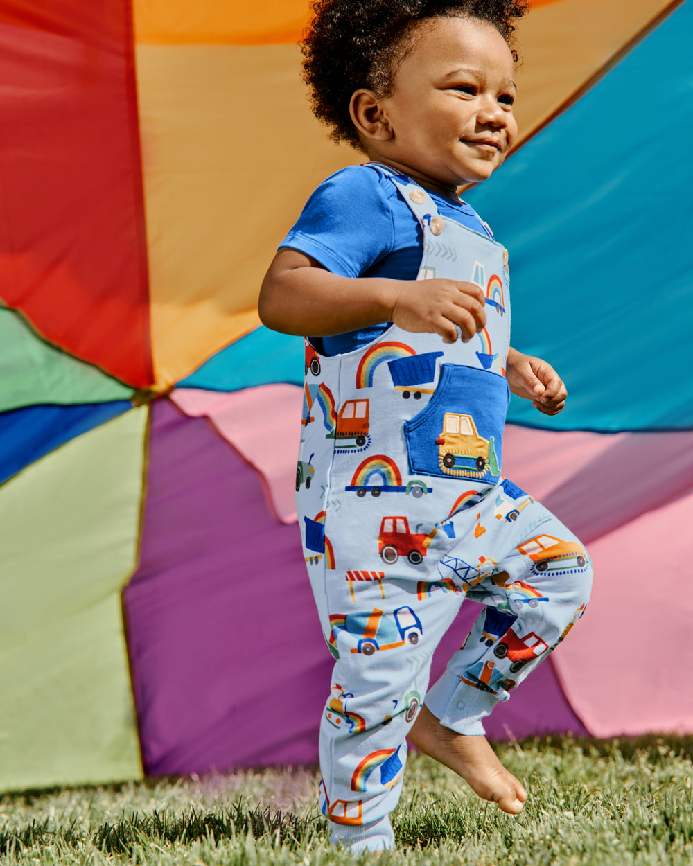 Boy walking on grass wearing the Rainbow Trucks Overall Set