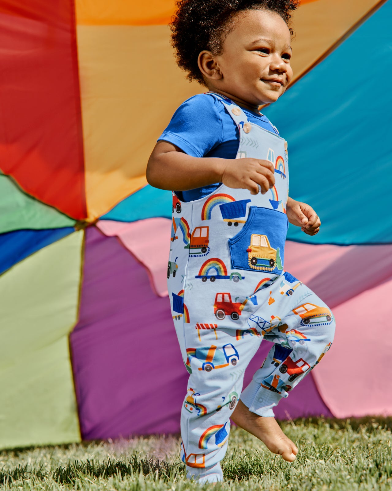 Boy walking on grass wearing the Rainbow Trucks Overall Set