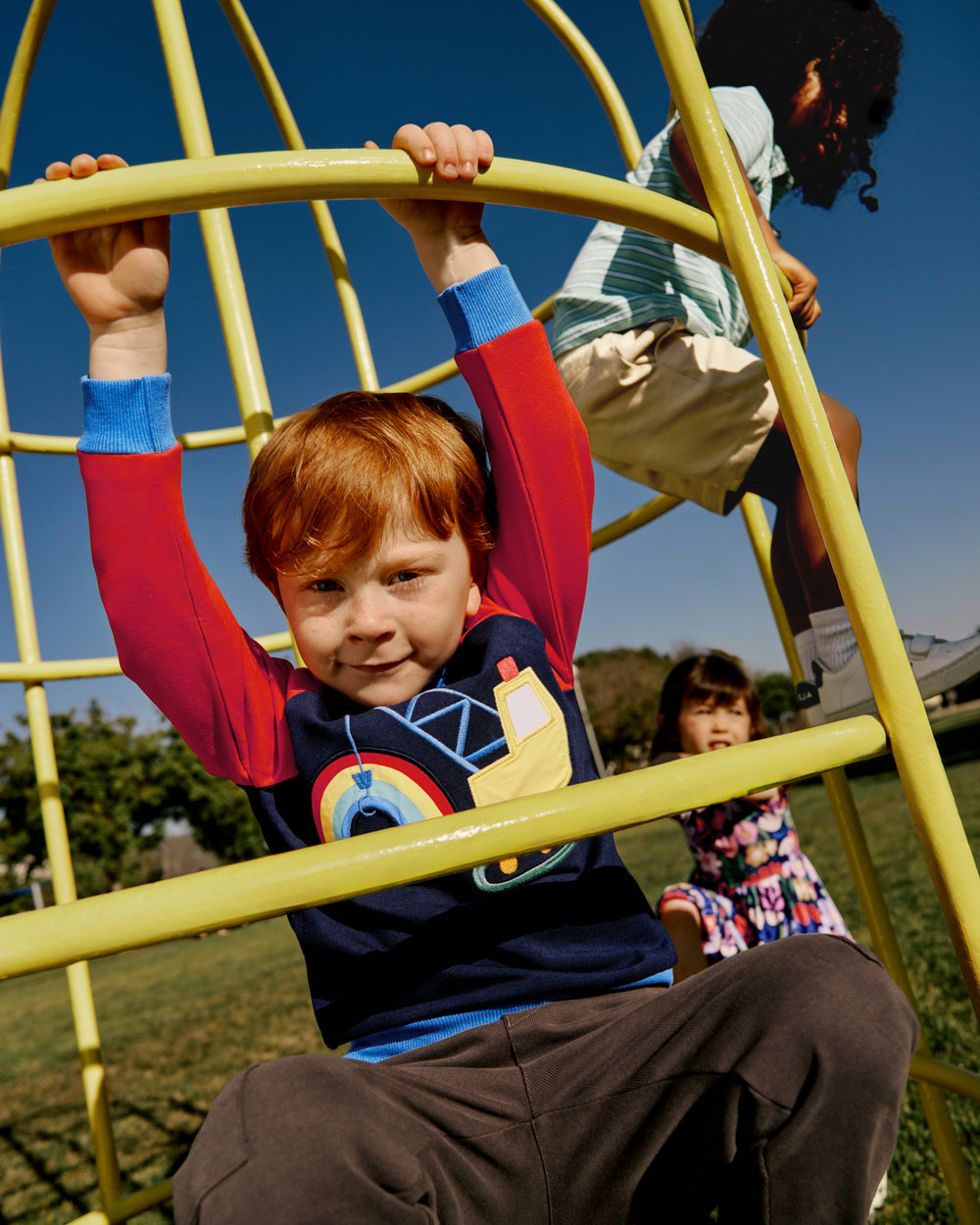 Boy wearing the Rainbow Trucks Crewneck Sweatshirt on a play scape 