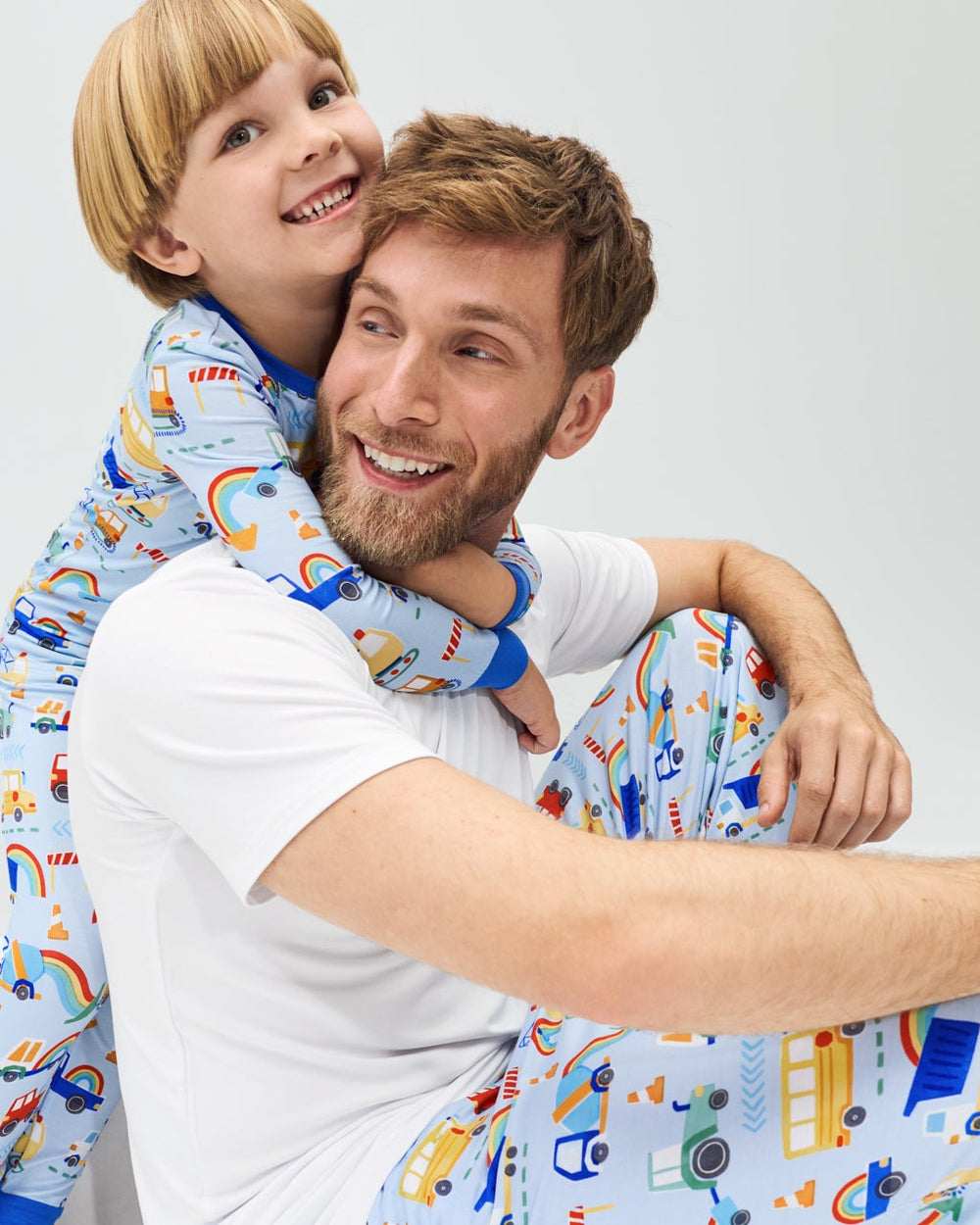 Father and son wearing matching Rainbow Trucks pajamas