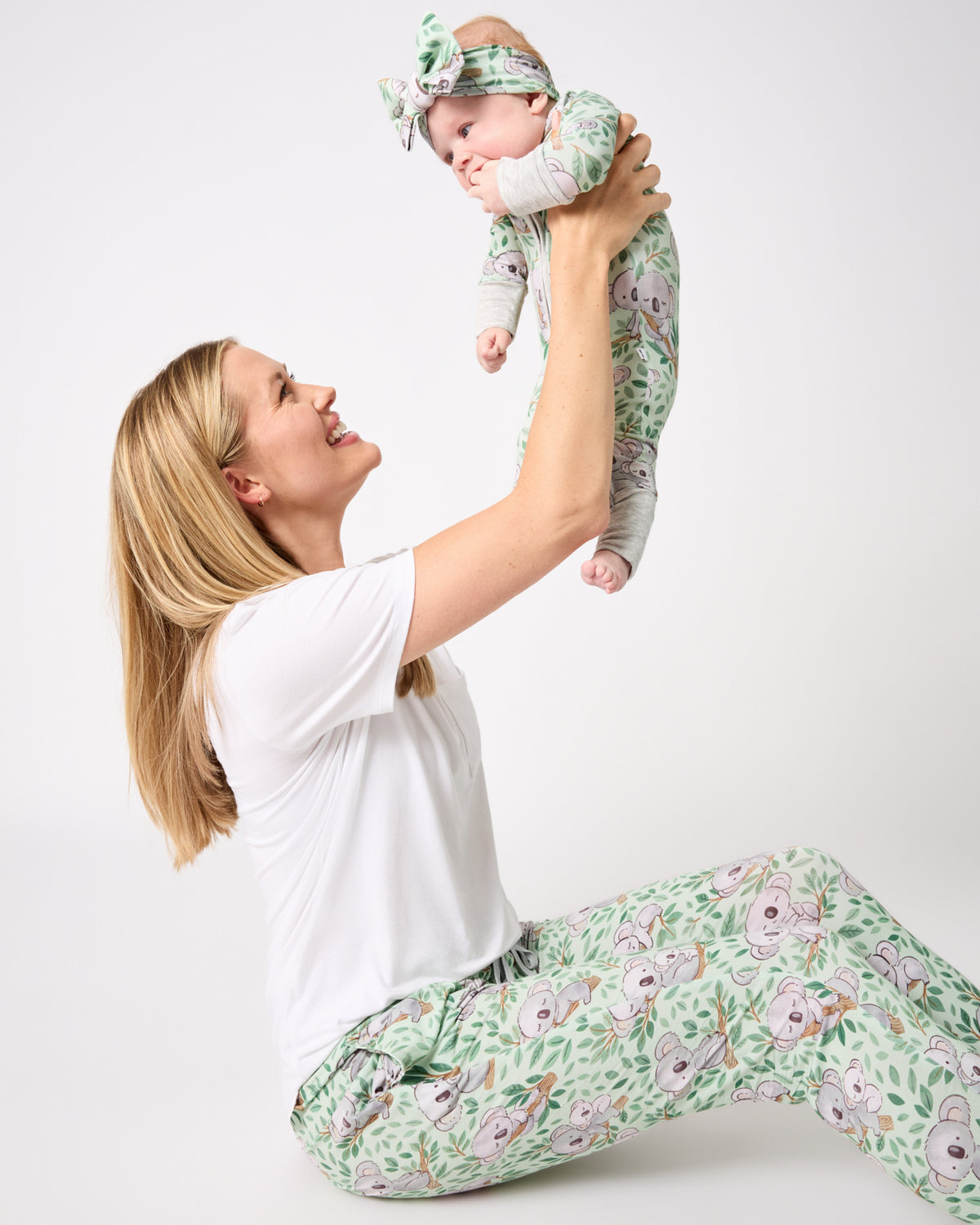 Woman wearing the Koala Cuddles Women's Pajama Pants holding a baby in a matching zippy