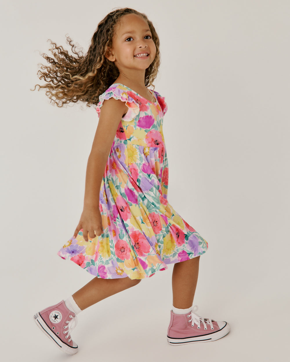 Child in motion wearing the Watercolor Meadow Flutter Twirl Dress with pink sneakers