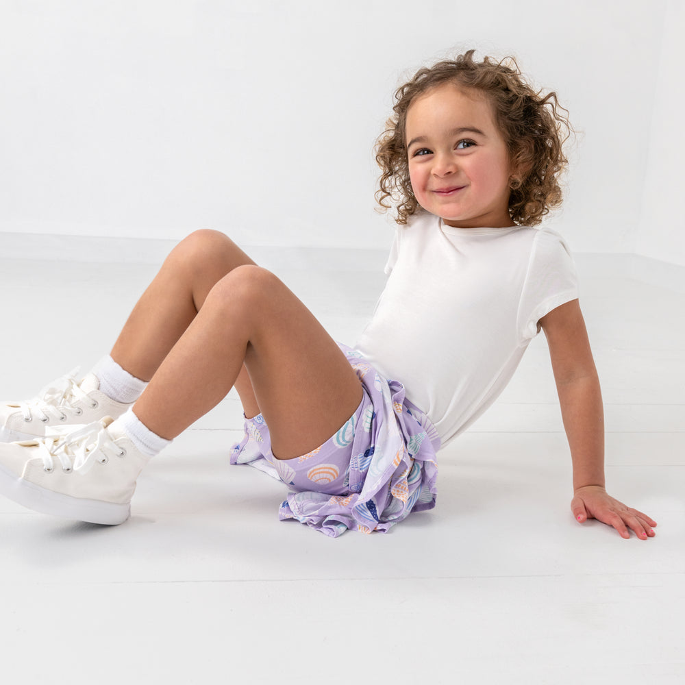 Sitting child wearing the Sandy Treasures Ruffle Skort with a white tee