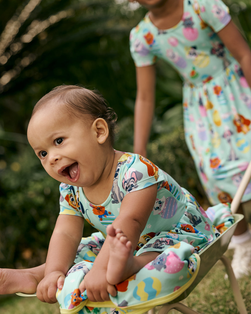 Baby wearing the Disney Peekaboo Pets Bow Back Skater Dress with Bodysuit sitting in a wheelbarrow 