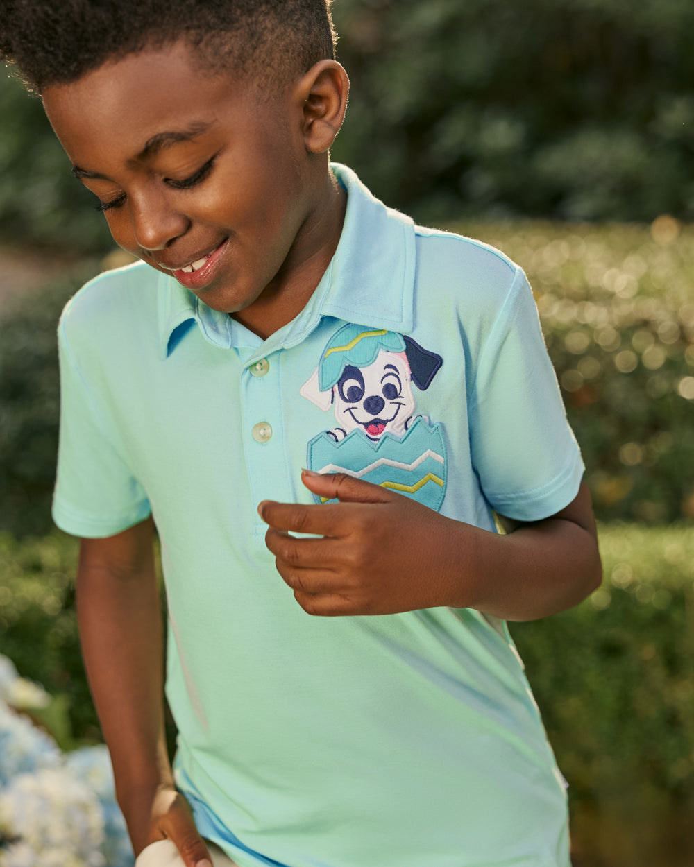 Close up of child wearing the Disney Peekaboo Pets Polo Shirt with greenery in the background