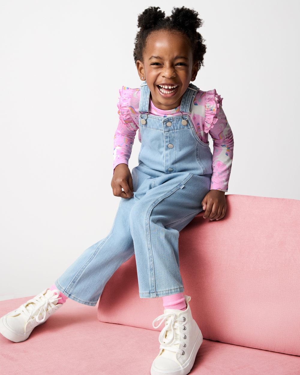 Girl wearing the Light Blue Denim Overall on a pink modular couch