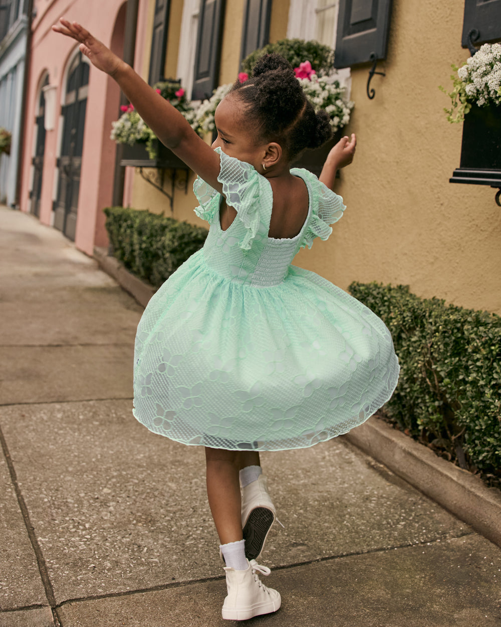 Dancing girl wearing the Butterfly Brook Smocked Flutter Dress with a cityscape in the background