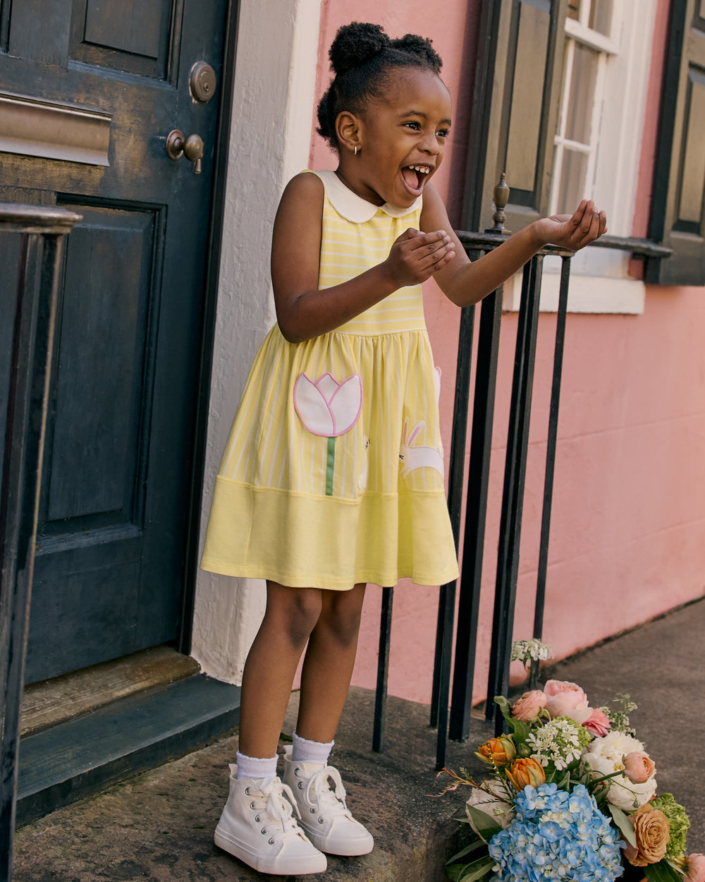 Girl wearing the Sunny Tulip Collar Skater Dress on the front steps of a pink house