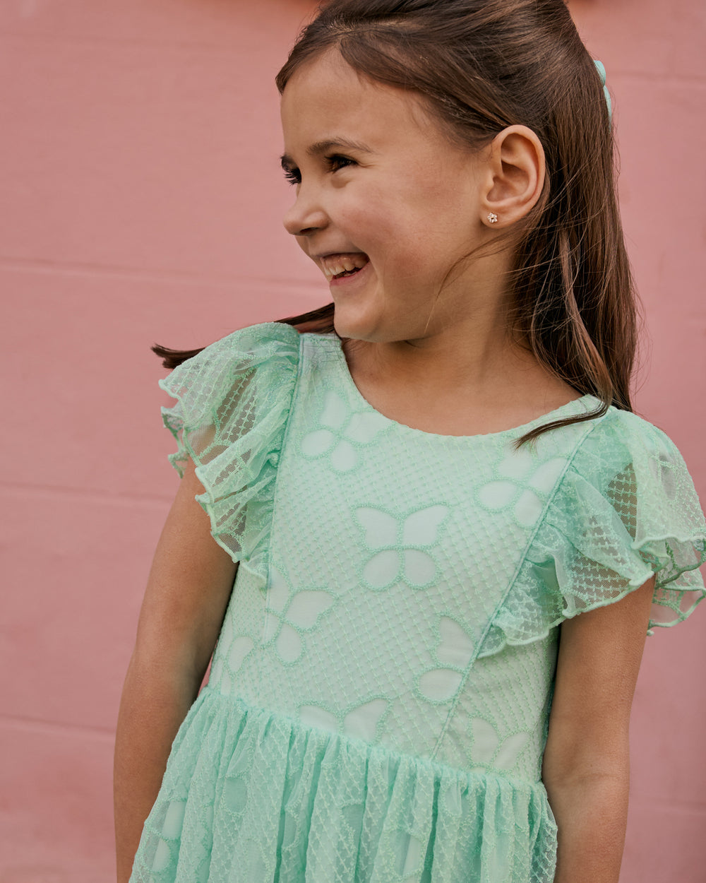 Close up of girl wearing the Butterfly Brook Smocked Flutter Dress on a pink background