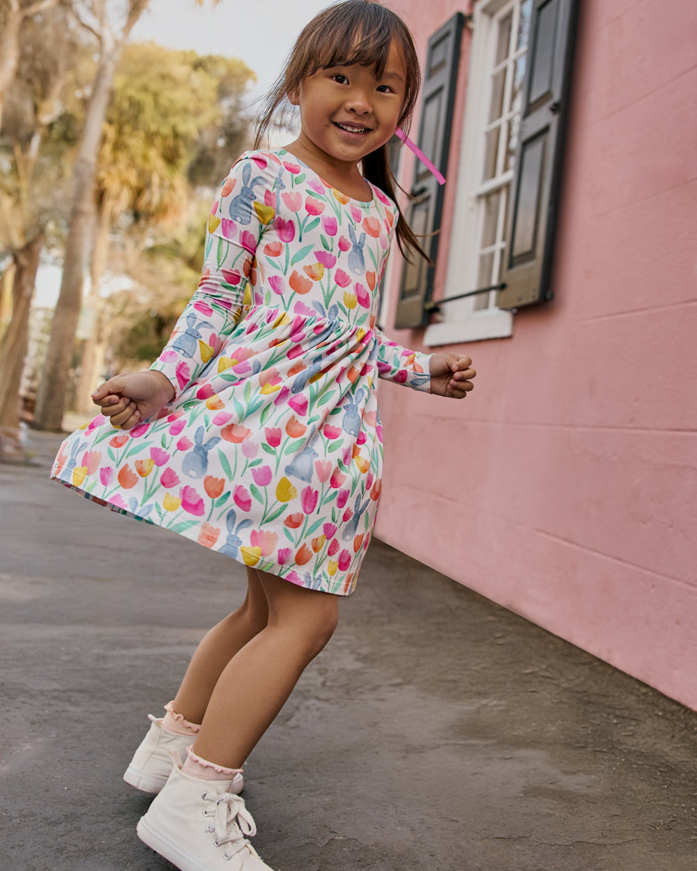 Girl wearing the Garden Hop Bow Back Skater Dress with a pink building in the background