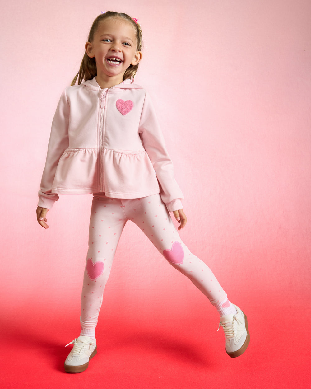 Girl wearing the Little Love Flare Zip Hoodie and Leggings on a red background