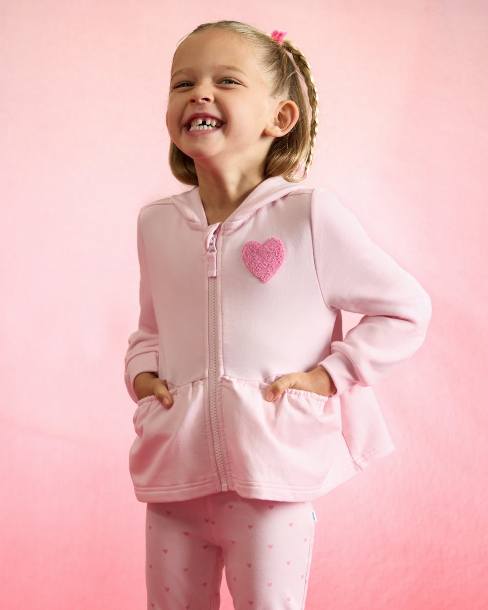 Girl wearing the Little Love Flare Zip Hoodie on a red background 