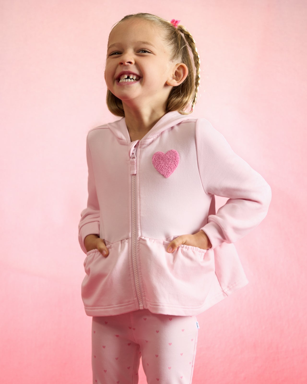 Girl wearing the Little Love Flare Zip Hoodie on a red background 
