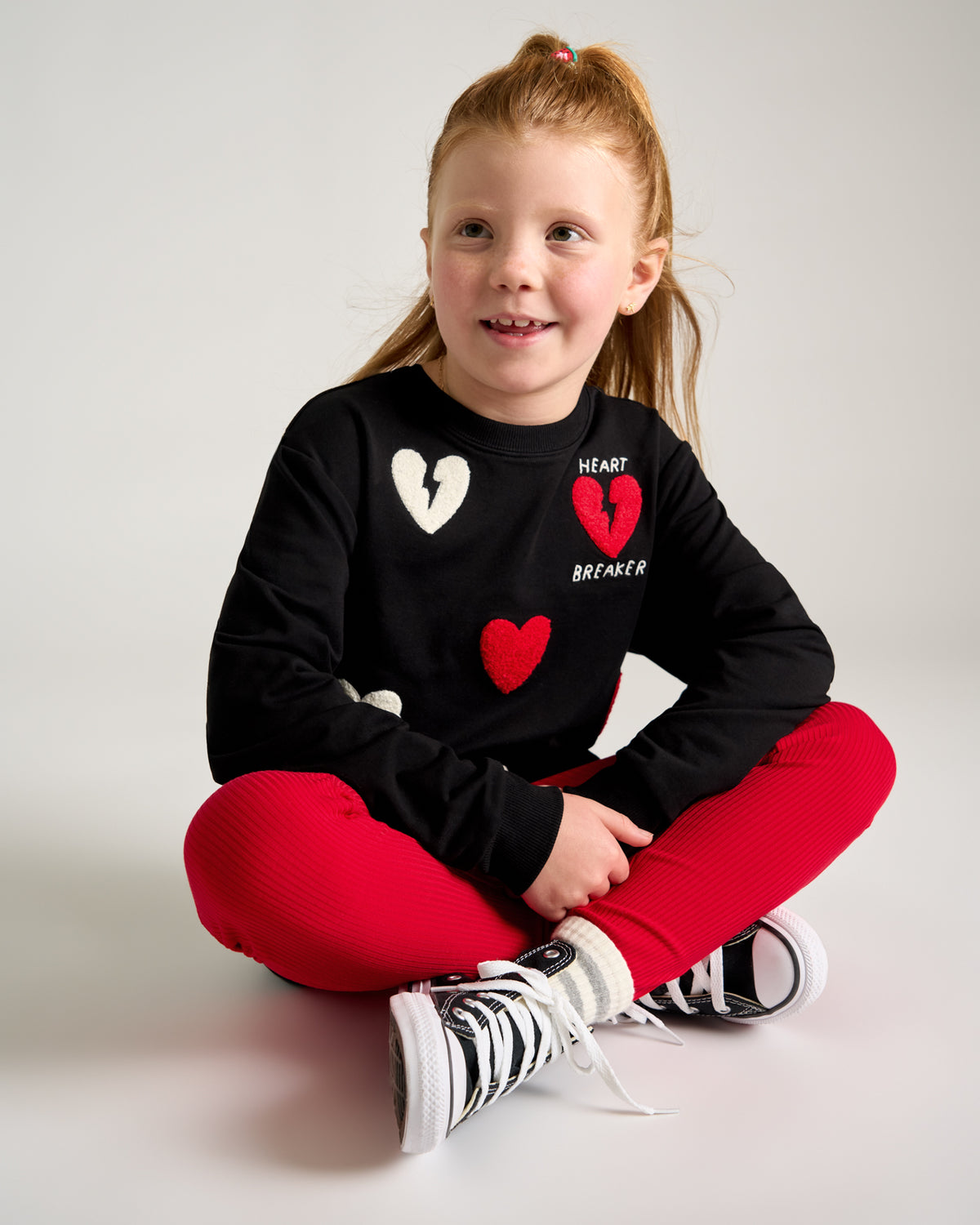 Sitting girl wearing the Candy Red Ribbed Legging and black crewneck