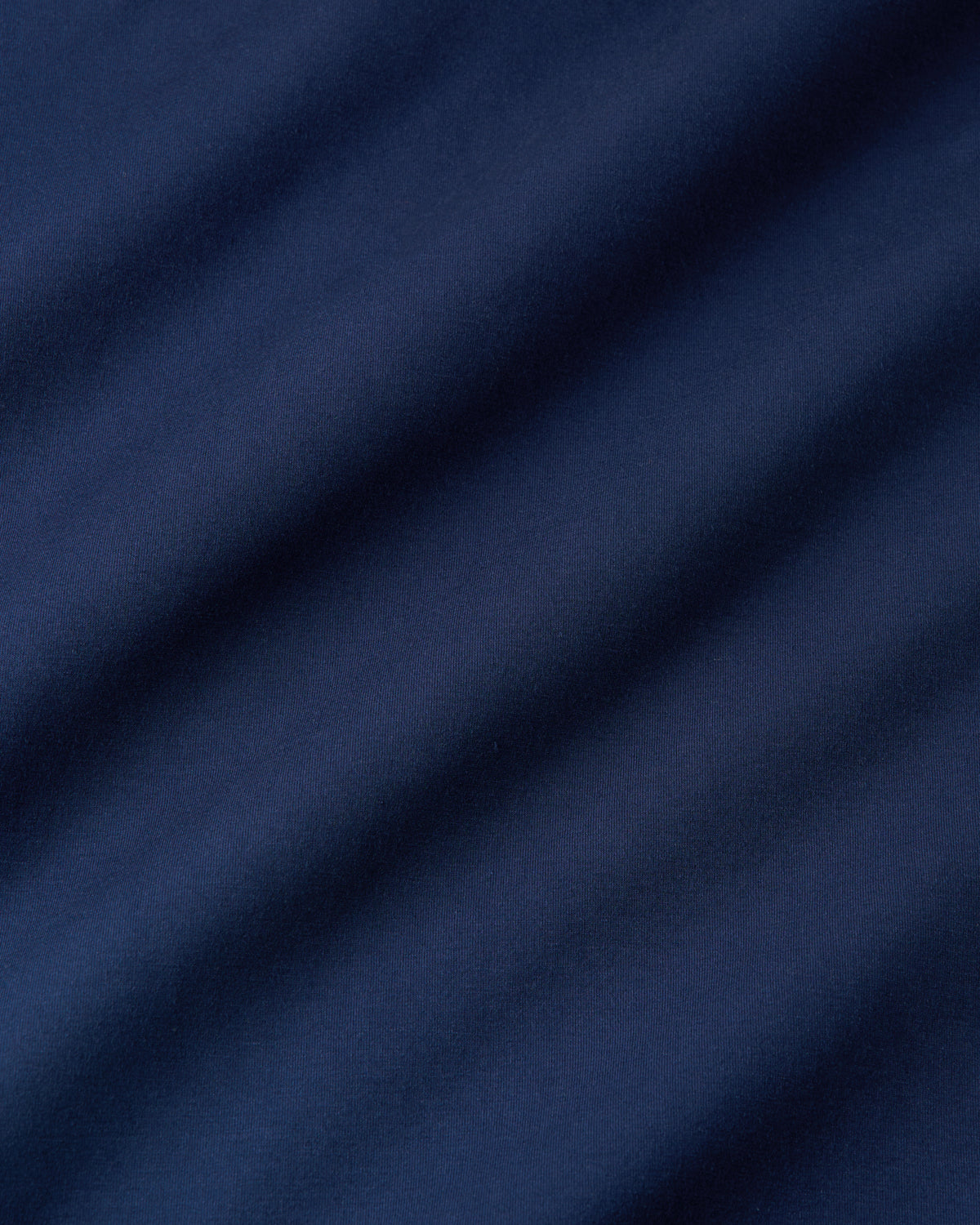 A close-up of dark navy blue fabric with soft diagonal folds and shadows.