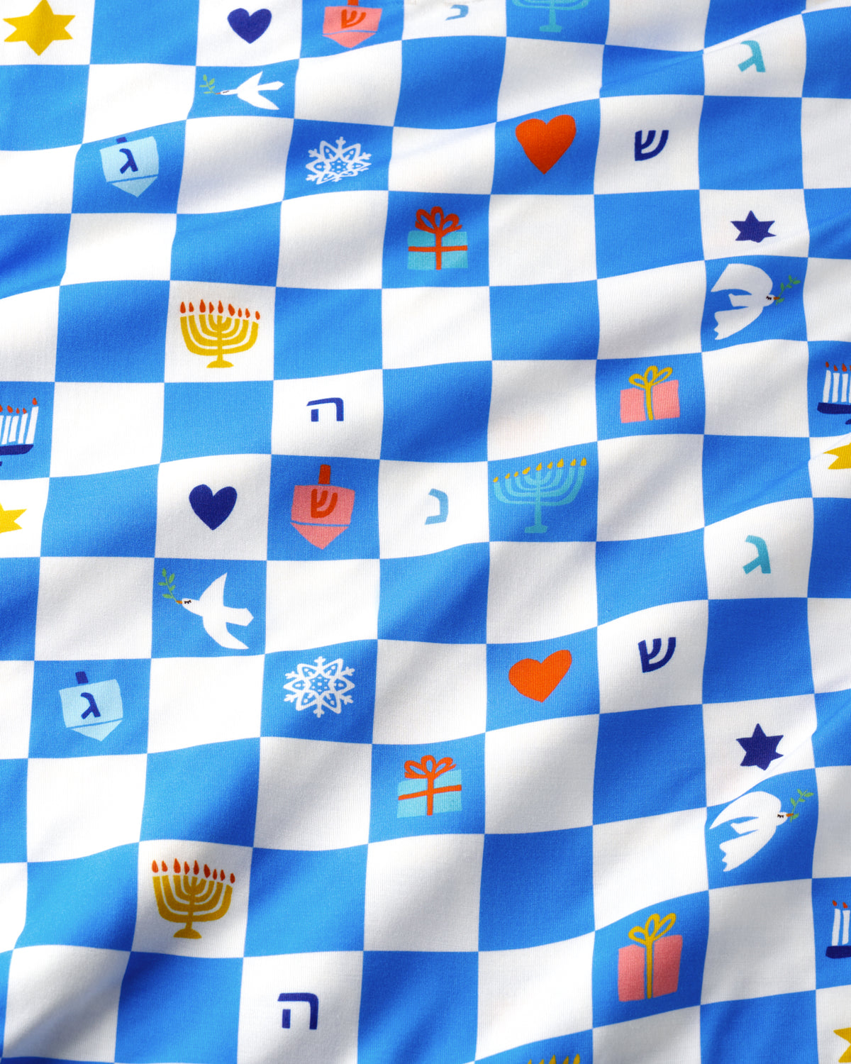 A close-up of a blue and white checkered fabric with small colorful holiday-themed icons and Hebrew letters printed across it.