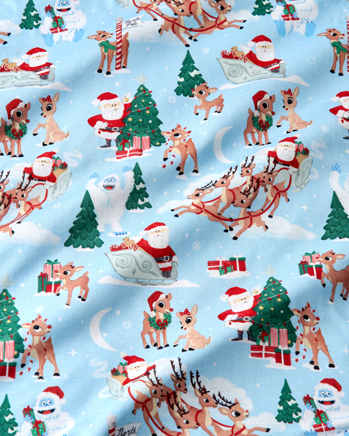 Light blue Christmas-themed fabric with a repeating pattern of Santa Claus in sleves, reindeer, Christmas trees, gifts, snowmen, and a crescent moon.