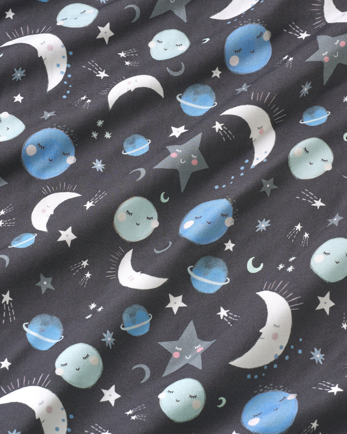 A close-up of a dark charcoal gray fabric with a whimsical celestial print featuring cute, sleeping cartoon planets, crescent moons, and stars in light blue, white, and gray.