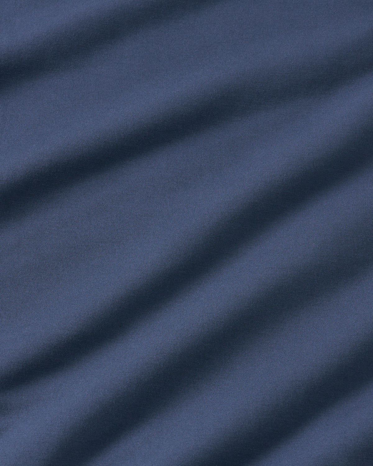 A close-up of dark navy blue fabric with soft diagonal folds and a fine woven texture.
