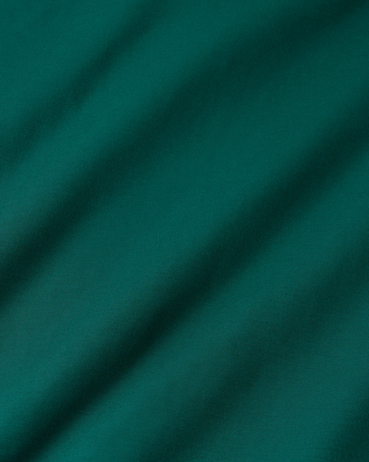 A close-up of green fabric with soft diagonal folds and shadows.