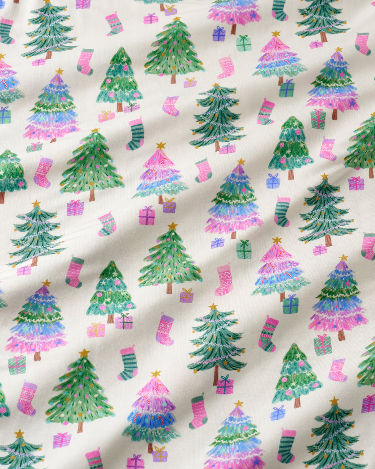 A close-up of a fabric or wallpaper pattern featuring watercolor-style Christmas trees, pink and green stockings, and wrapped gifts on an off-white background.