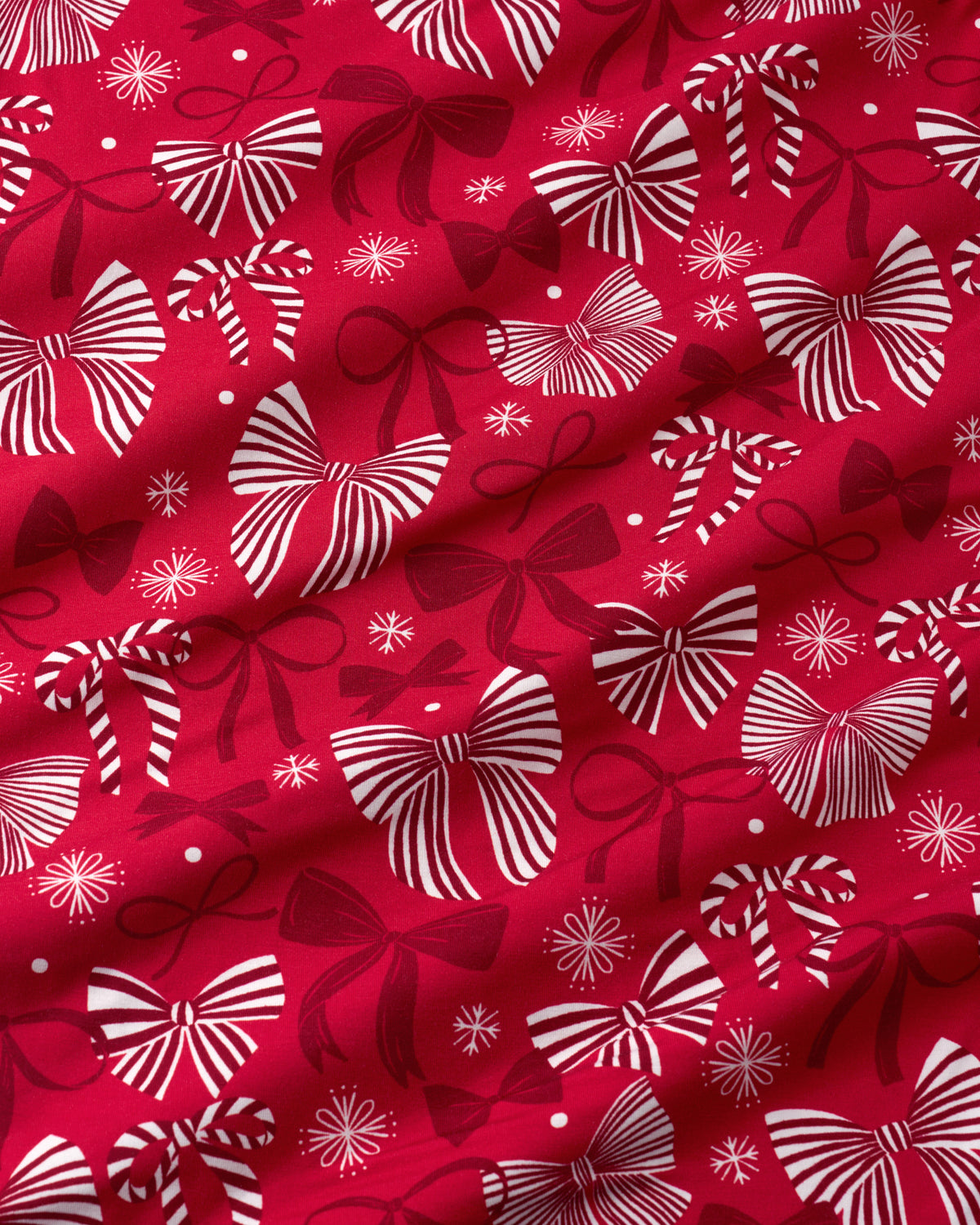 Red fabric with a repeating pattern of white and dark red striped gift bows and small snowflake-like motifs.