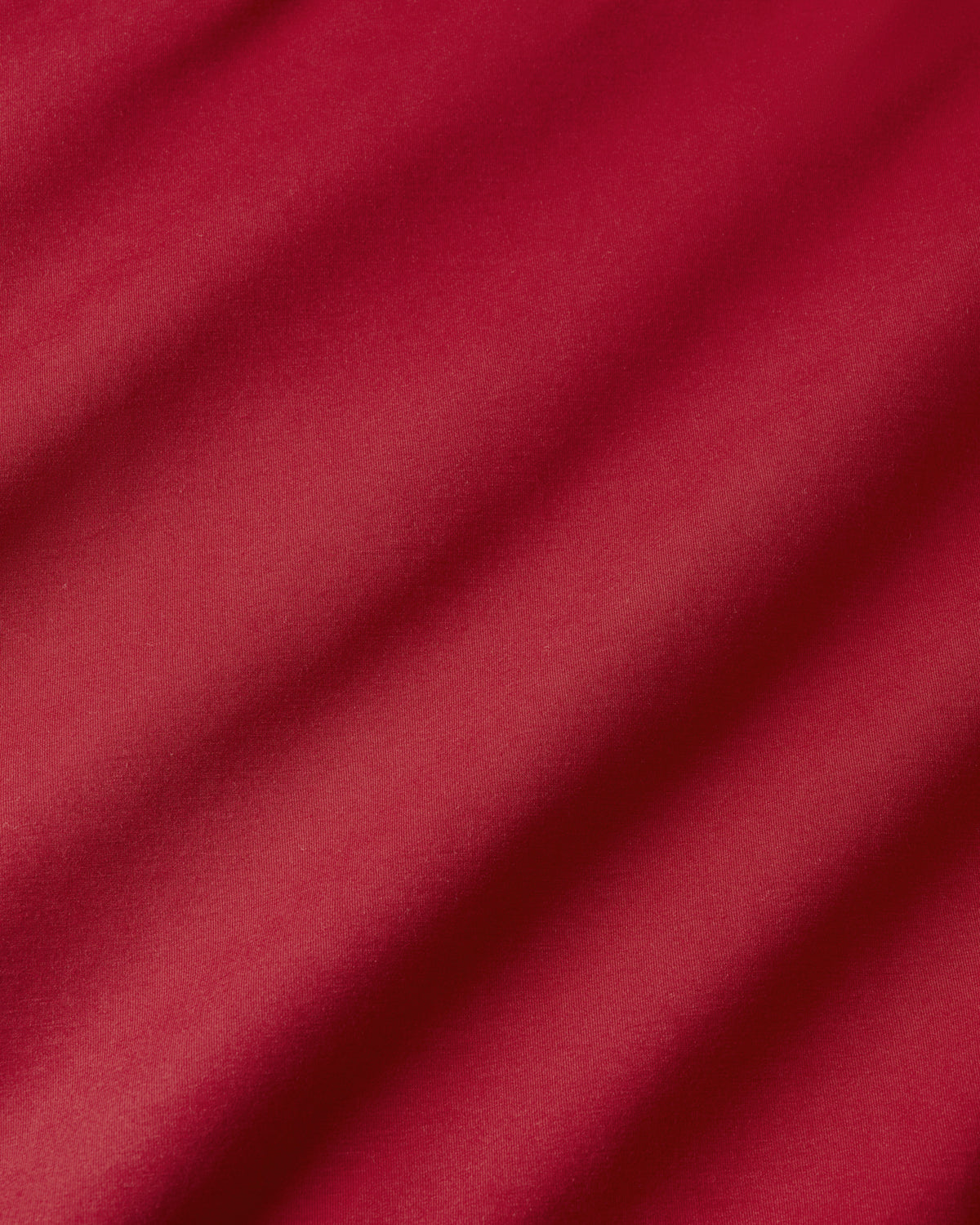 A close-up of draped red fabric with soft diagonal folds and a smooth texture.