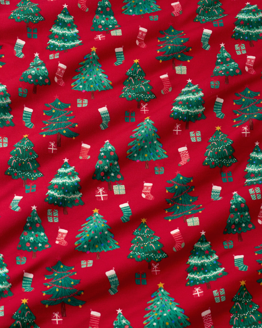 Red fabric with a repeating Christmas tree pattern in green, decorated with small stockings, gifts, and stars.