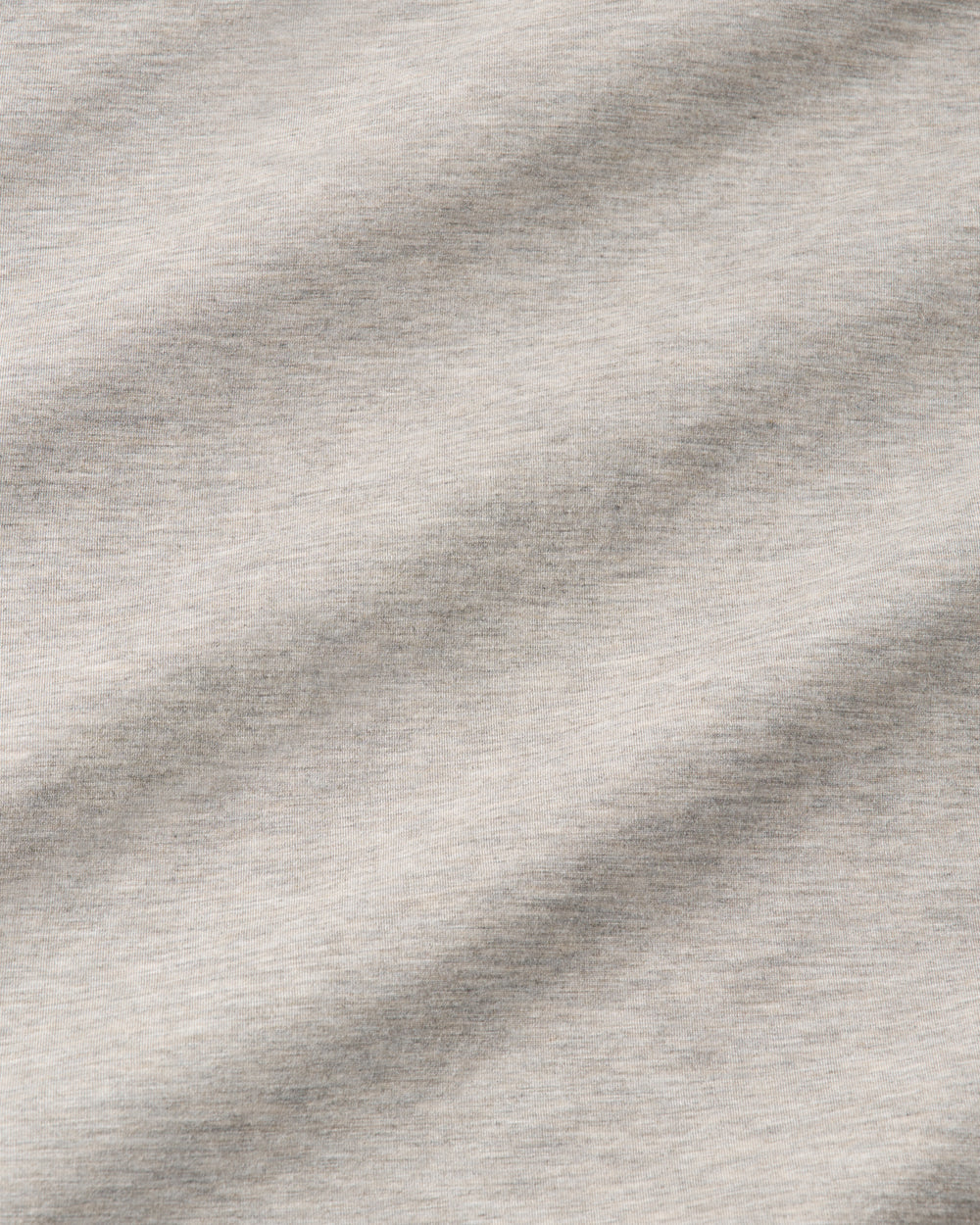A close-up of a light heather gray fabric texture with soft diagonal folds and shadows.