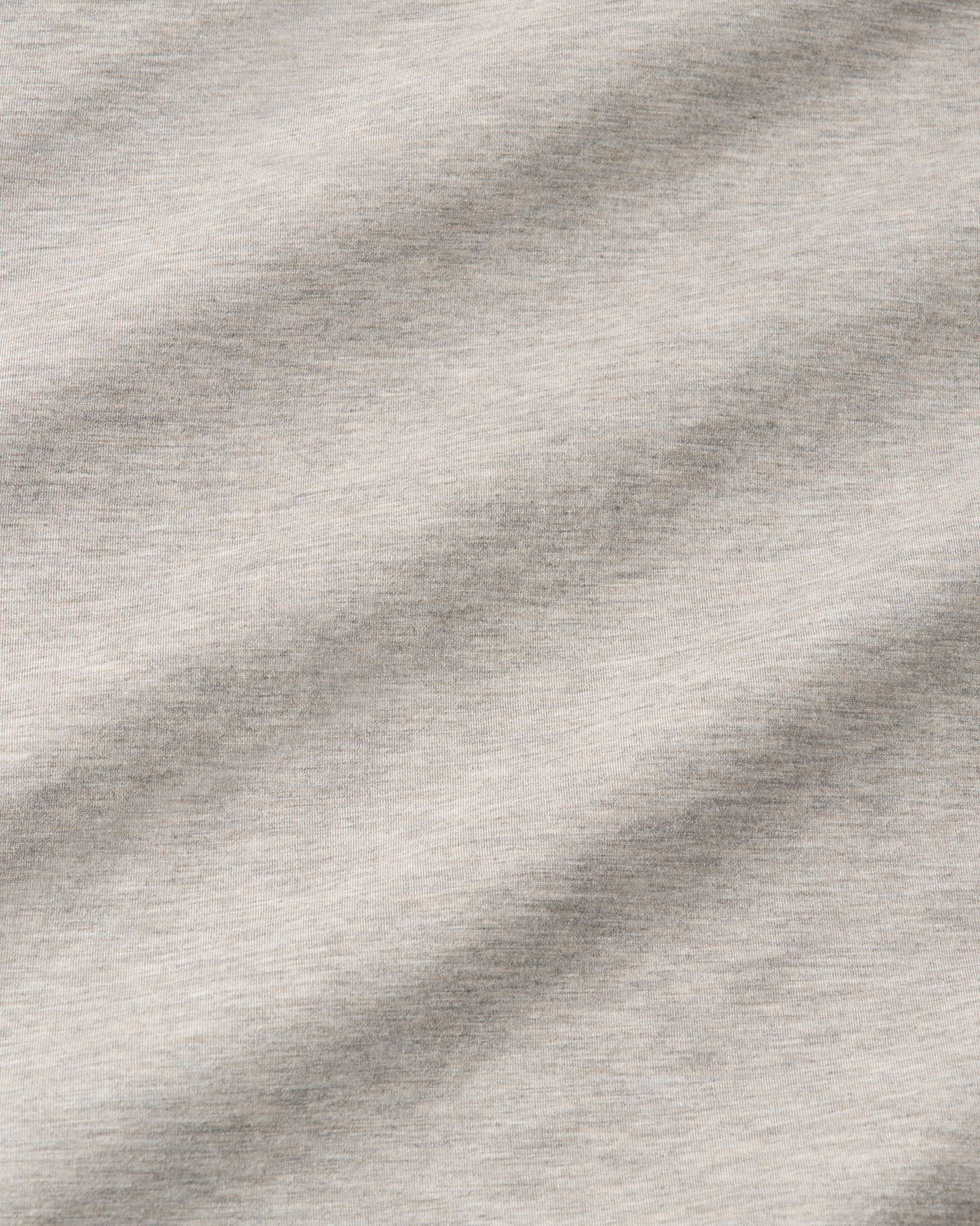 A close-up of a light heather gray fabric texture with soft diagonal folds and shadows.