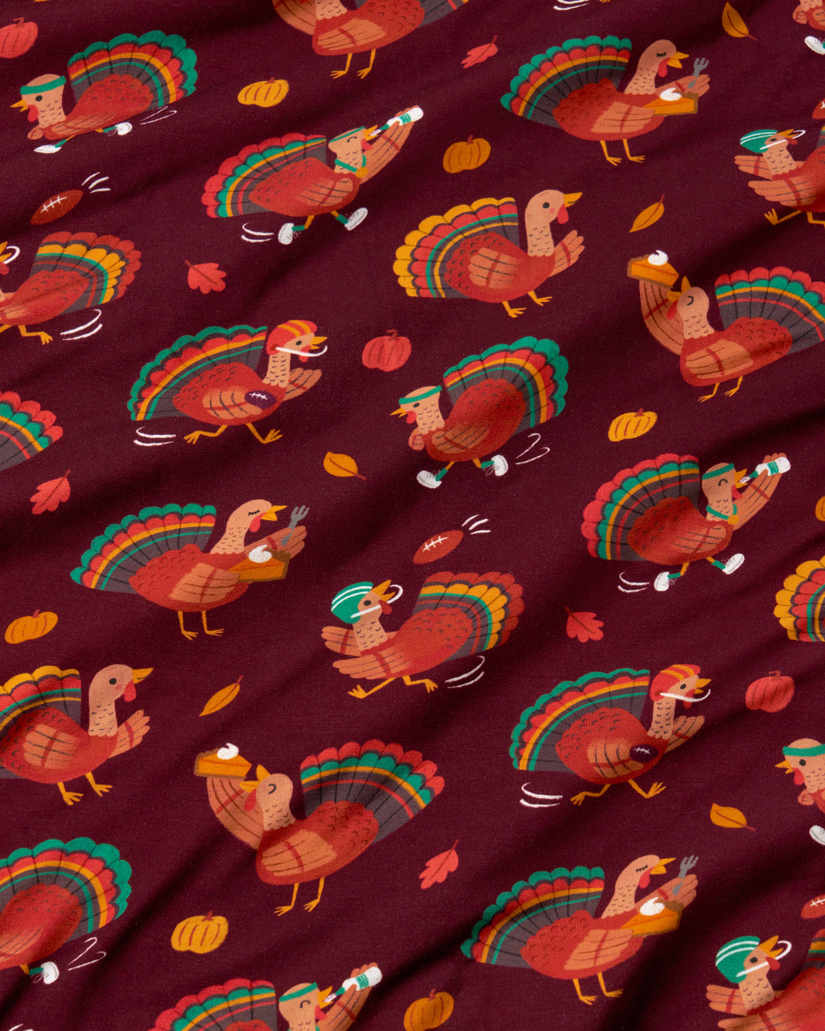 A close-up of a fabric with a repeating Thanksgiving turkey pattern on a deep burgundy background. The fabric features stylized turkeys in orange, brown, and green, along with small pumpkins and autumn leaves.