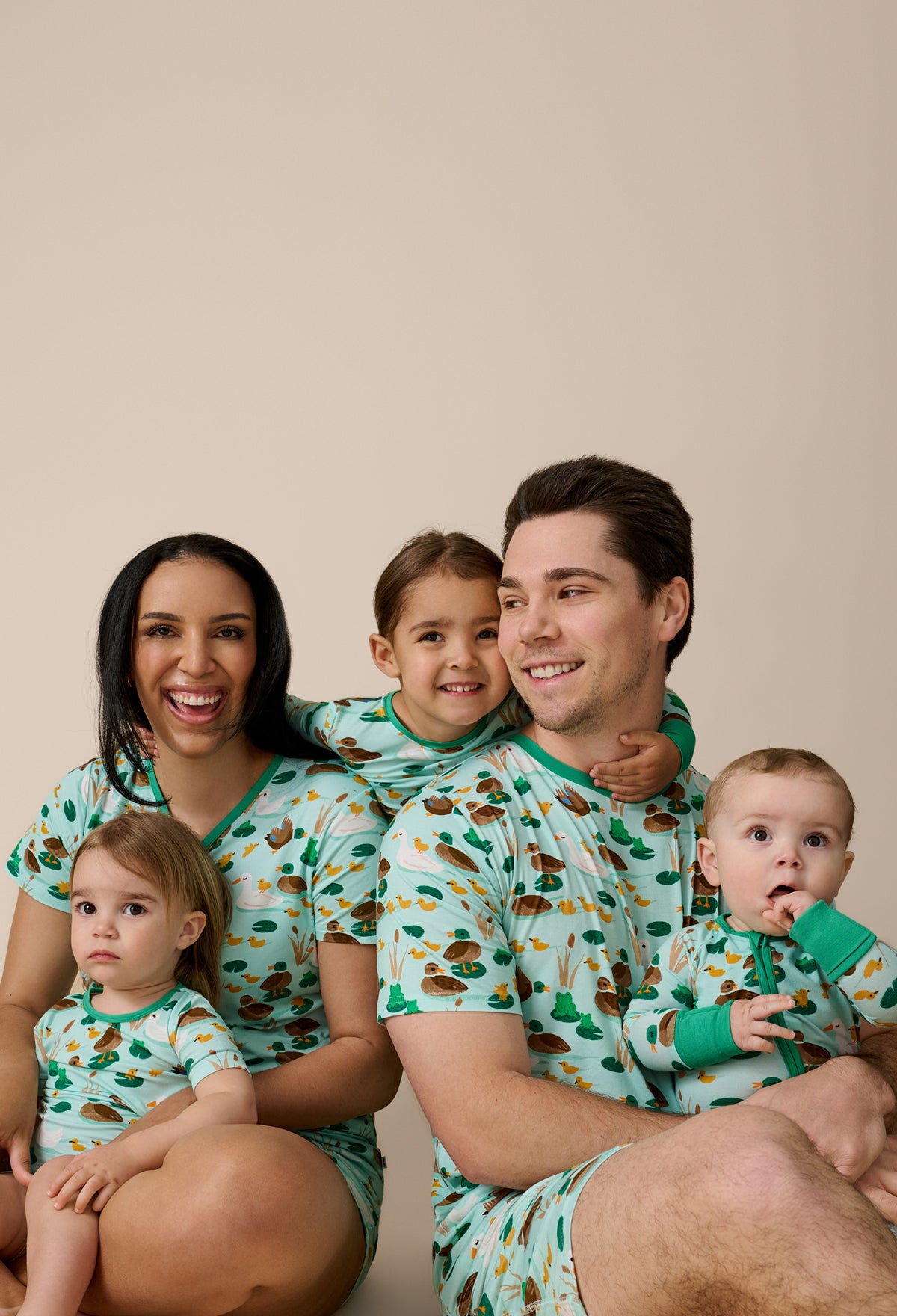 Family of five wearing matching pajamas with a duck pattern on a beige background