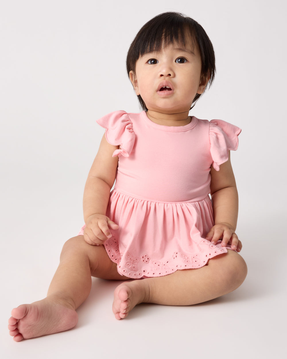 Sitting baby wearing the Soft Coral Puff Sleeve Eyelet Bodysuit