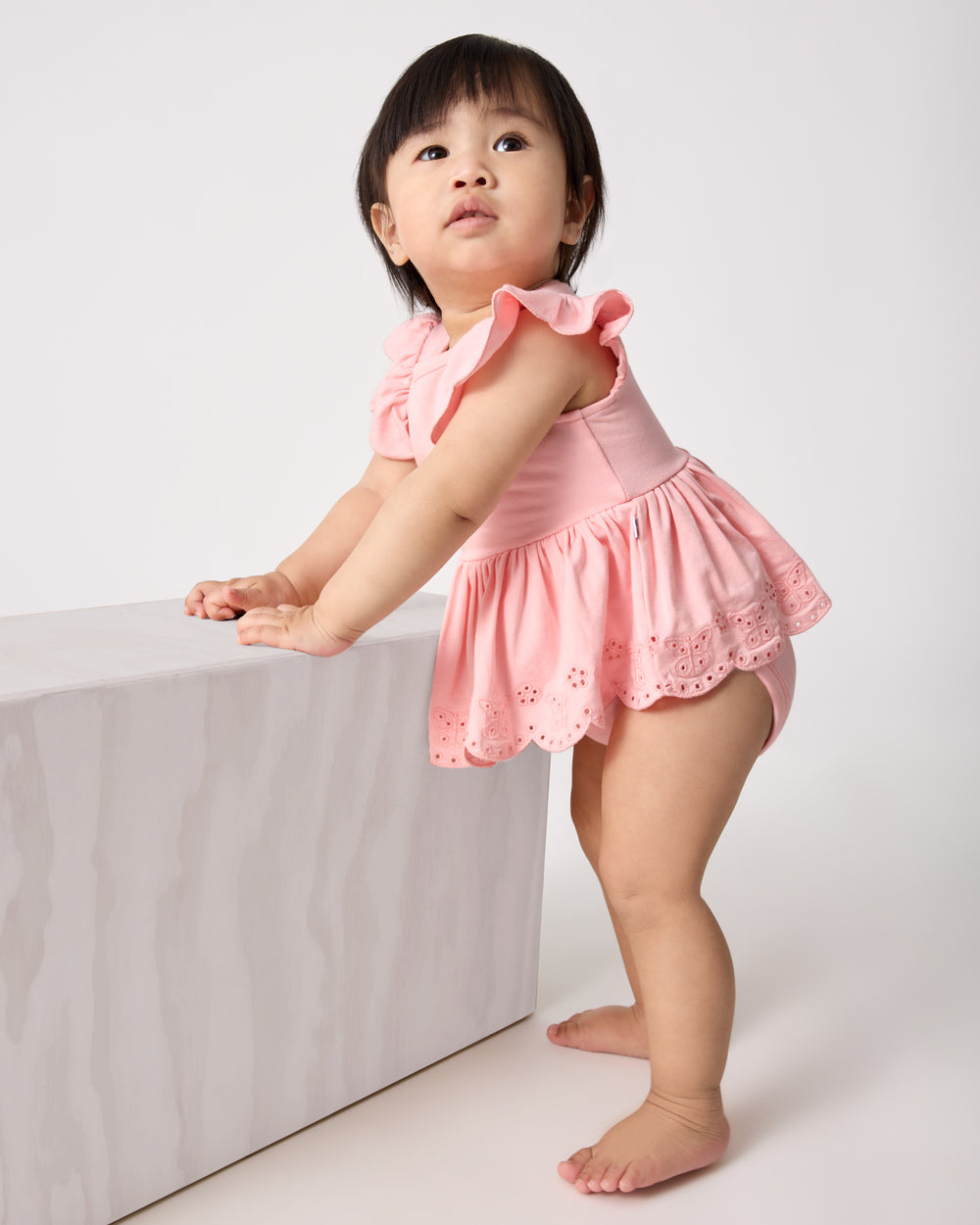 Standing baby wearing the Soft Coral Puff Sleeve Eyelet Bodysuit