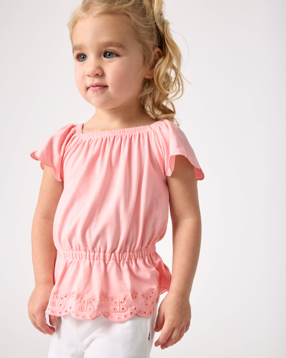 Alternate child wearing the Soft Coral Puff Sleeve Eyelet Top with white shorts