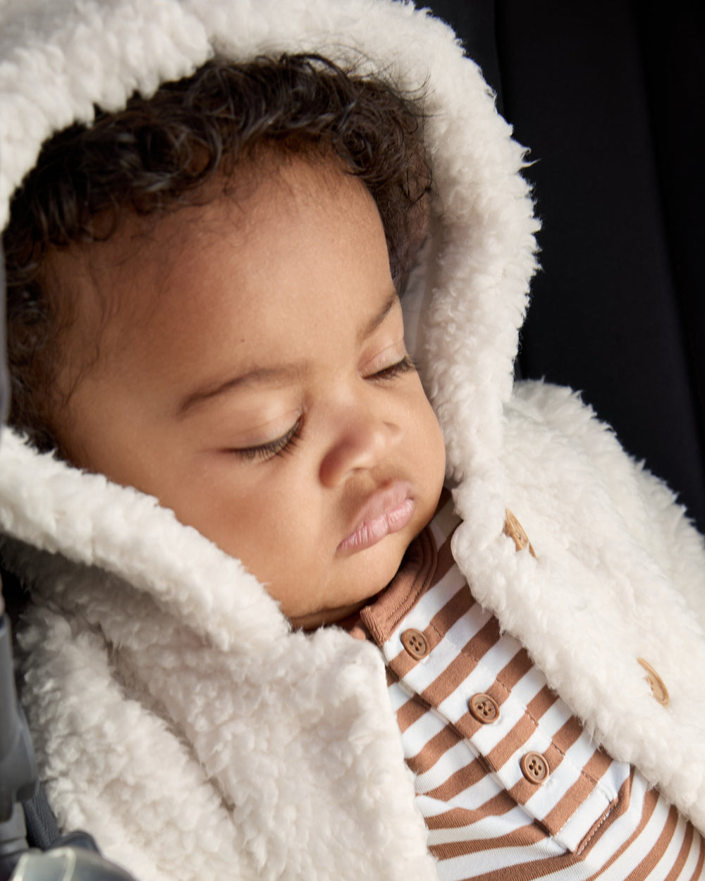 Close up of baby in a stroller wearing the Soft White Sherpa Baby Jacket