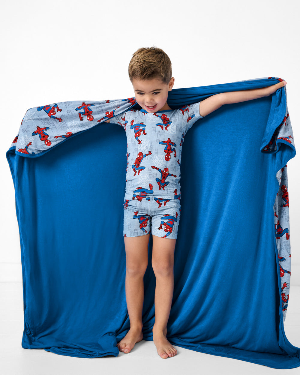 Standing boy holding up the Spidey Sense Large Cloud Blanket® showing the solid blue side